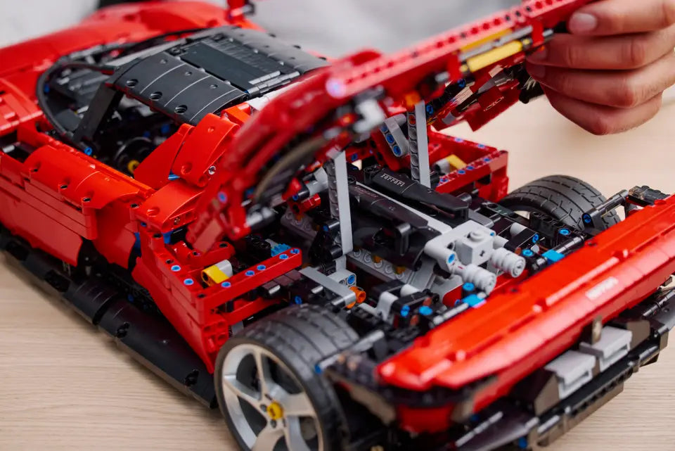 Close-up of a red and black LEGO Technic model car being assembled on a wooden surface.